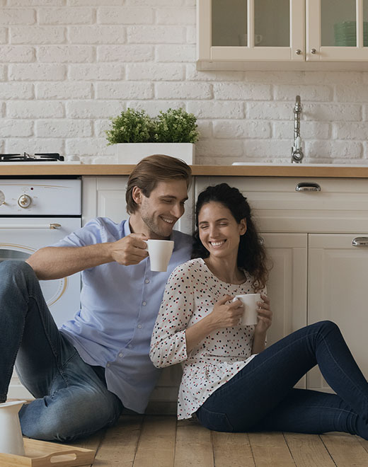A couple drinks coffee while sitting on their kitchen floor. A couple drinks coffee while sitting on their kitchen floor.