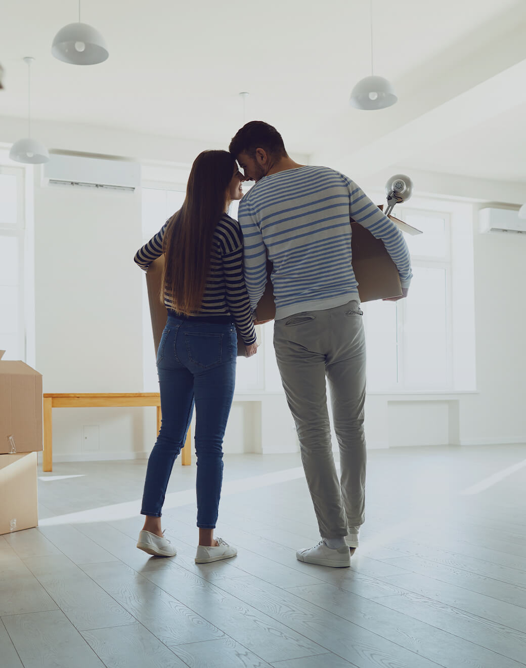 A couple holding moving boxes in a mostly empty room.