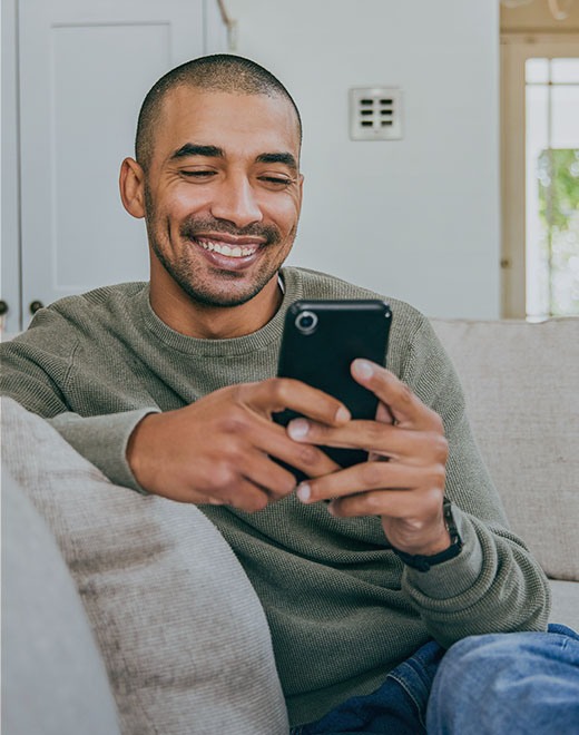 A young man sitting casually on a couch smiles while holding his smart phone. A young man sitting casually on a couch smiles while holding his smart phone.